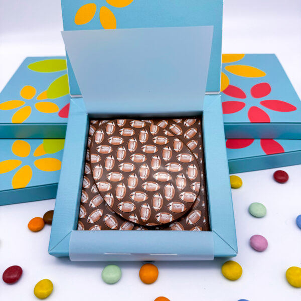 A delicious Milk Chocolate Rugby Easter Egg surprise for Easter morning. A flat milk chocolate egg laid on top of a milk chunky square, both decorated with rugby balls.