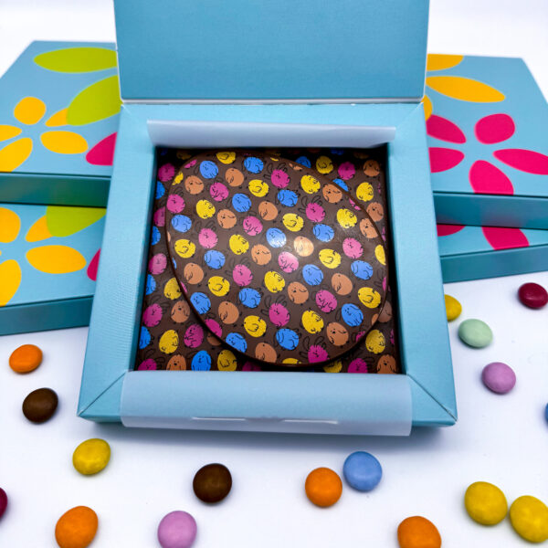 A flat Milk Chocolate Easter Egg on top of a solid square of milk chocolate. Both decorated with an Easter pattern.